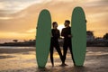 Happy millennial couple with surfboards standing on the beach on sunset time Royalty Free Stock Photo