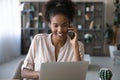 Smiling ethnic woman work on laptop talk on smartphone call