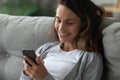 Happy millennial girl relax on couch using cellphone Royalty Free Stock Photo