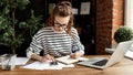 Happy millennial woman taking notes in notepad while working at laptop in comfortable loft office