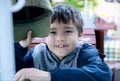 Happy mixed race boy holding cap hat and looking at camera with smiling face, Smile young kid waiting for lunch at outdoor cafe Royalty Free Stock Photo