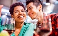 Happy mixed race couple of lovers drinking red wine at fancy winery bar - Handsome man whispers soft kisses in beautiful woman ear Royalty Free Stock Photo