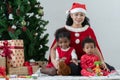 Little African kids and Asian young mother in Santa Claus cloth sitting together on floor with Christmas tree and gift box at home