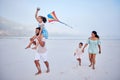 Happy mixed race family running along the beach with a kite. Carefree parents and two children enjoying fun activity Royalty Free Stock Photo