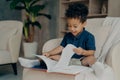 Happy mixed race little kid with cute curly hair reading book at home Royalty Free Stock Photo