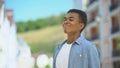 Happy mixed-race male teen inhaling pleasant bakery aroma on city street, joy