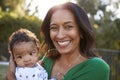 Happy African American middle aged grandmother holding her three month old grandson in the garden and smiling to camera, close up