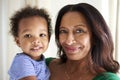 Happy African American middle aged grandmother holding her two year old grandson, both looking to camera smiling, close up, head 