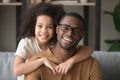 Happy mixed-race preschool girl embracing black father looking at camera