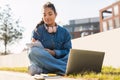 Happy mixed race teen lady writing something in notebook, sitting with laptop computer in park, studying outdoors Royalty Free Stock Photo