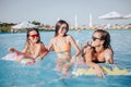 Happy models are in swimming pool. They pose on camera. Two models are lying on floats and look at woman in middle. She