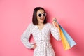 Happy modern asian woman going shopping in malls, holding bags with clothes and smiling, wearing sunglasses, standing Royalty Free Stock Photo