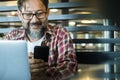 Happy modern mature man at work in coworking workplace alternative office using laptop computer and mobile phone to communicate. Royalty Free Stock Photo