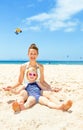 Happy modern mother and child in beachwear sitting on seashore