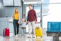 Happy mom and dad holding hands with daughter and standing with suitcases near gate Royalty Free Stock Photo