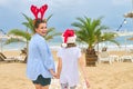 Happy mom and daughter child in Santa hat walking along beach, back view Royalty Free Stock Photo