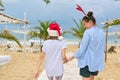 Happy mom and daughter child in Santa hat walking along beach, back view Royalty Free Stock Photo