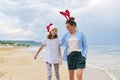 Happy mom and daughter child in Santa hat walking along beach Royalty Free Stock Photo