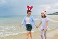 Happy mom and daughter child in Santa hat walking along beach Royalty Free Stock Photo