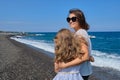 Happy mom and daughter kid hugging walking together along the beach, back view Royalty Free Stock Photo