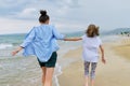 Happy mom and daughter running on the sea beach holding hands, back view Royalty Free Stock Photo