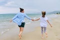 Happy mom and daughter running on the sea beach holding hands, back view Royalty Free Stock Photo