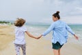 Happy mom and daughter running on the sea beach holding hands, back view Royalty Free Stock Photo