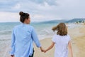 Happy mom and daughter walking on the sea beach holding hands, back view Royalty Free Stock Photo