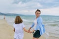 Happy mom and daughter walking on the sea beach holding hands, back view Royalty Free Stock Photo