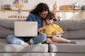 Mom embracing preschool kid playing games on tablet during break from remote work on laptop computer Royalty Free Stock Photo