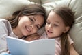 Happy mom listening child daughter learning reading book in bed Royalty Free Stock Photo