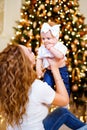 Happy mom playing with little cute baby daughter while sitting near Christmas tree in living room Royalty Free Stock Photo