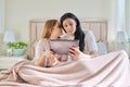 Happy mom and preteen daughter hugging together looking at screen of digital tablet Royalty Free Stock Photo