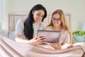 Happy mom and preteen daughter hugging together looking at screen of digital tablet Royalty Free Stock Photo