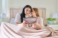 Happy mom and preteen daughter hugging together looking at screen of digital tablet Royalty Free Stock Photo