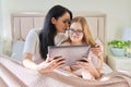 Happy mom and preteen daughter hugging together looking at screen of digital tablet Royalty Free Stock Photo