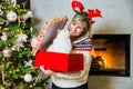 Happy mom with reindeers horns on the top of the head opening the gift with ragdoll cat by the Christmas tree and shining fireplac Royalty Free Stock Photo