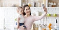 Happy mom taking photo with baby on smartphone at kitchen Royalty Free Stock Photo