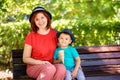 Happy mom and toddler child in blue hats sit on brown wooden bench in park, kid is holding ice-cream Royalty Free Stock Photo