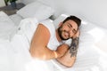 Happy morning. Satisfied guy waking up, feeling rested, happy bearded black guy lying on white linen flax bedsheets Royalty Free Stock Photo