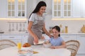 Happy mother adding milk to daughter`s cereal in kitchen. Single parenting Royalty Free Stock Photo