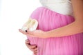 Happy mother in anticipation of the birth of daughter. Pregnant woman holding baby booties sneakers on tummy background. Close-up Royalty Free Stock Photo