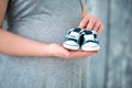 Happy mother in anticipation of the birth of her son. Pregnant woman holding baby booties sneakers on tummy background. Close-up Royalty Free Stock Photo