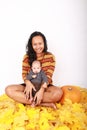 Happy mother and baby boy sitting on maple leaves by pumpkin Royalty Free Stock Photo