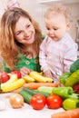 Happy mother with baby daughter preparing vegetables