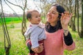 happy mother and baby daughter standing together under a tree in the countryside, smiling with love and affection. A perfect