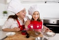 Happy mother baking with little daughter in apron and cook hat with flour dough at kitchen Royalty Free Stock Photo