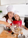 Happy mother baking with little daughter in apron and cook hat with flour dough at kitchen Royalty Free Stock Photo