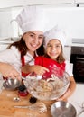 Happy mother baking with little daughter in apron and cook hat mixing flour at kitchen Royalty Free Stock Photo