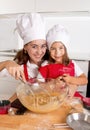 Happy mother baking with little daughter in apron and cook hat preparing dough at kitchen Royalty Free Stock Photo